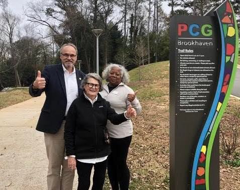 A man and two women standing next to the PCG Brookhaven sign with thumbs up.